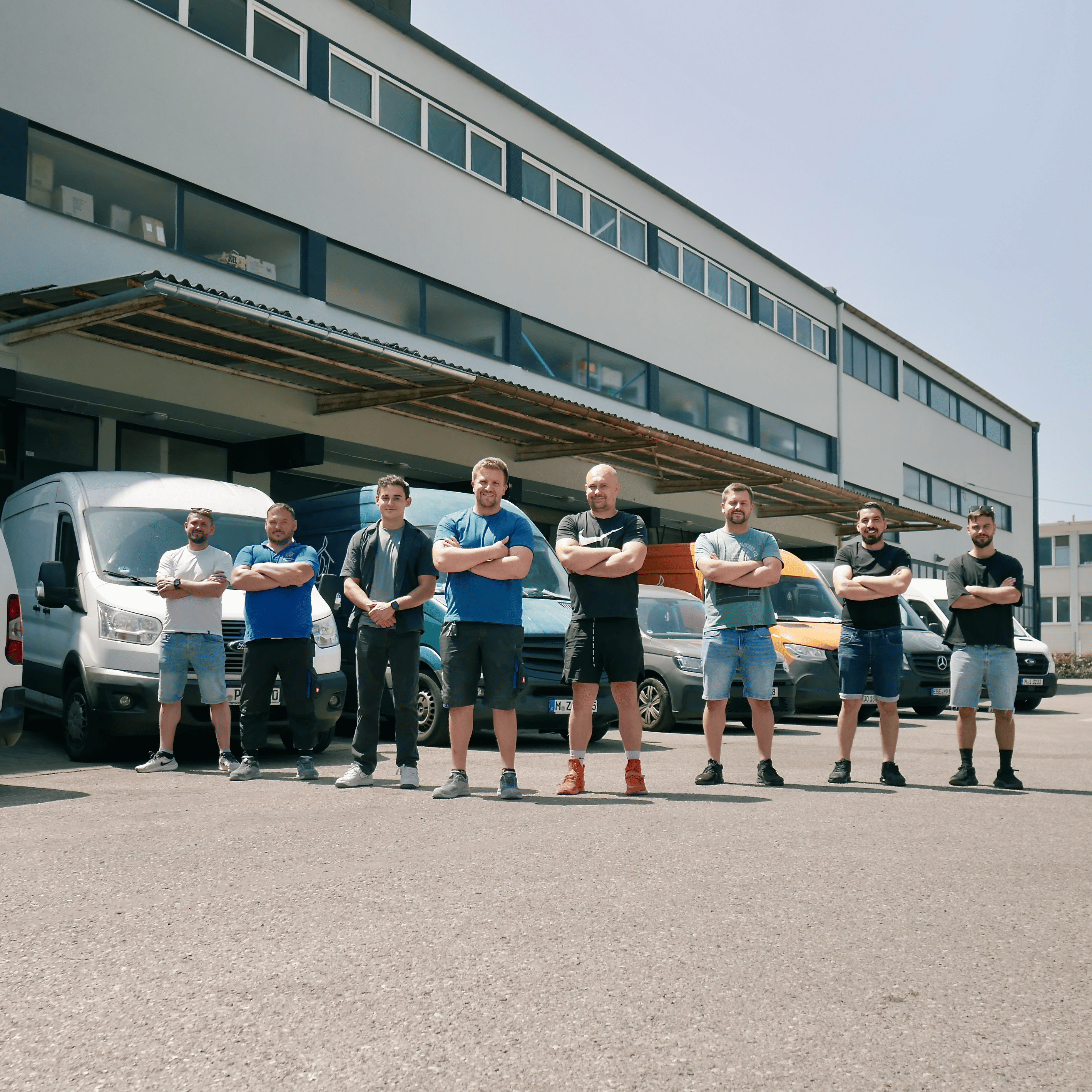 Menschen in einer Reihe, dass Team der Gebäudetechnik Bauer, im Hintergrund sind Fahrzeuge und ein Gebäude zu erkennen.
